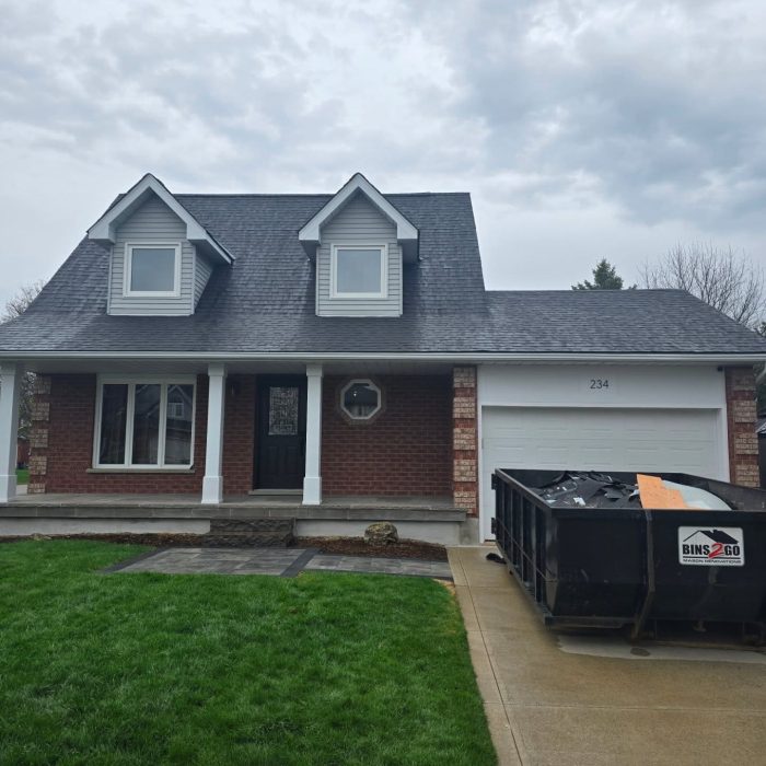 House with a steep roof and a Bins 2 Go disposal bin in the driveway, set against a cloudy sky.