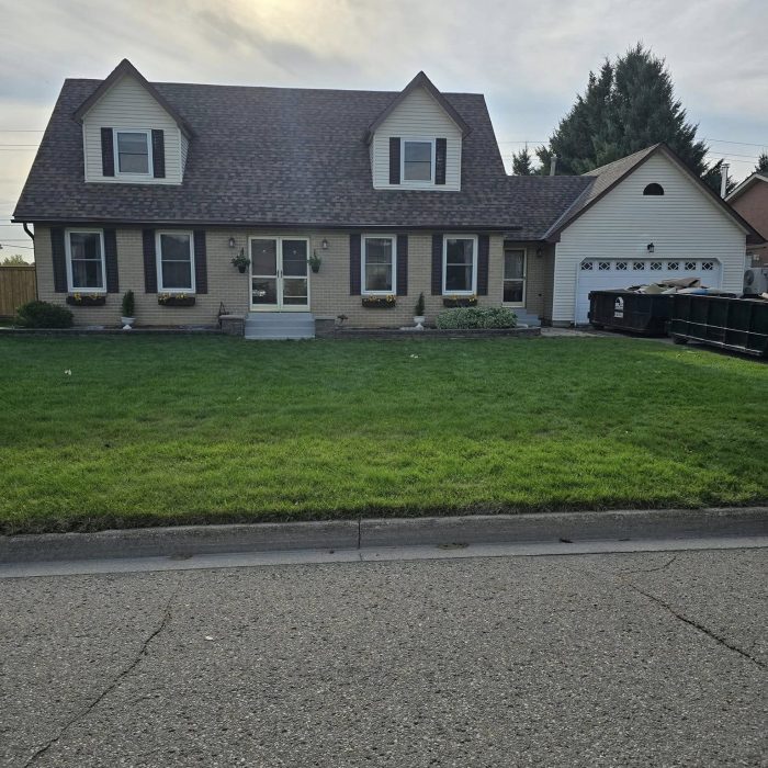 Sunny day over a charming suburban brick home with a well-kept lawn and attached garage.