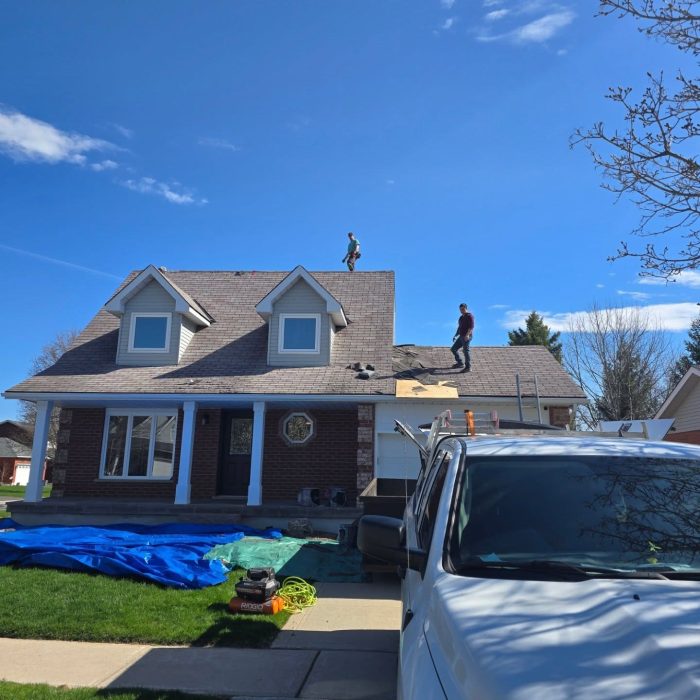 Roofers work on a residential home under a clear sky, ensuring quality roofing solutions.
