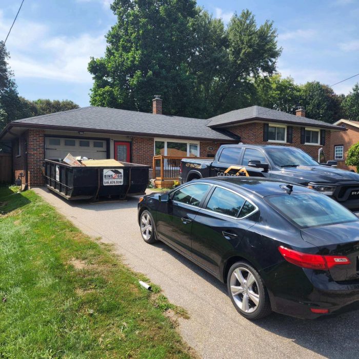 Driveway with a dumpster and parked vehicles in front of a brick house, ideal for home renovation projects.