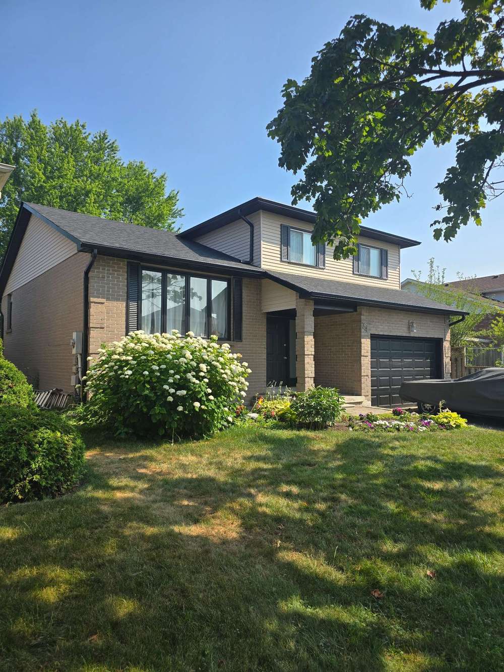 Suburban home with manicured lawn and blooming flowers under clear skies, perfect for family living.