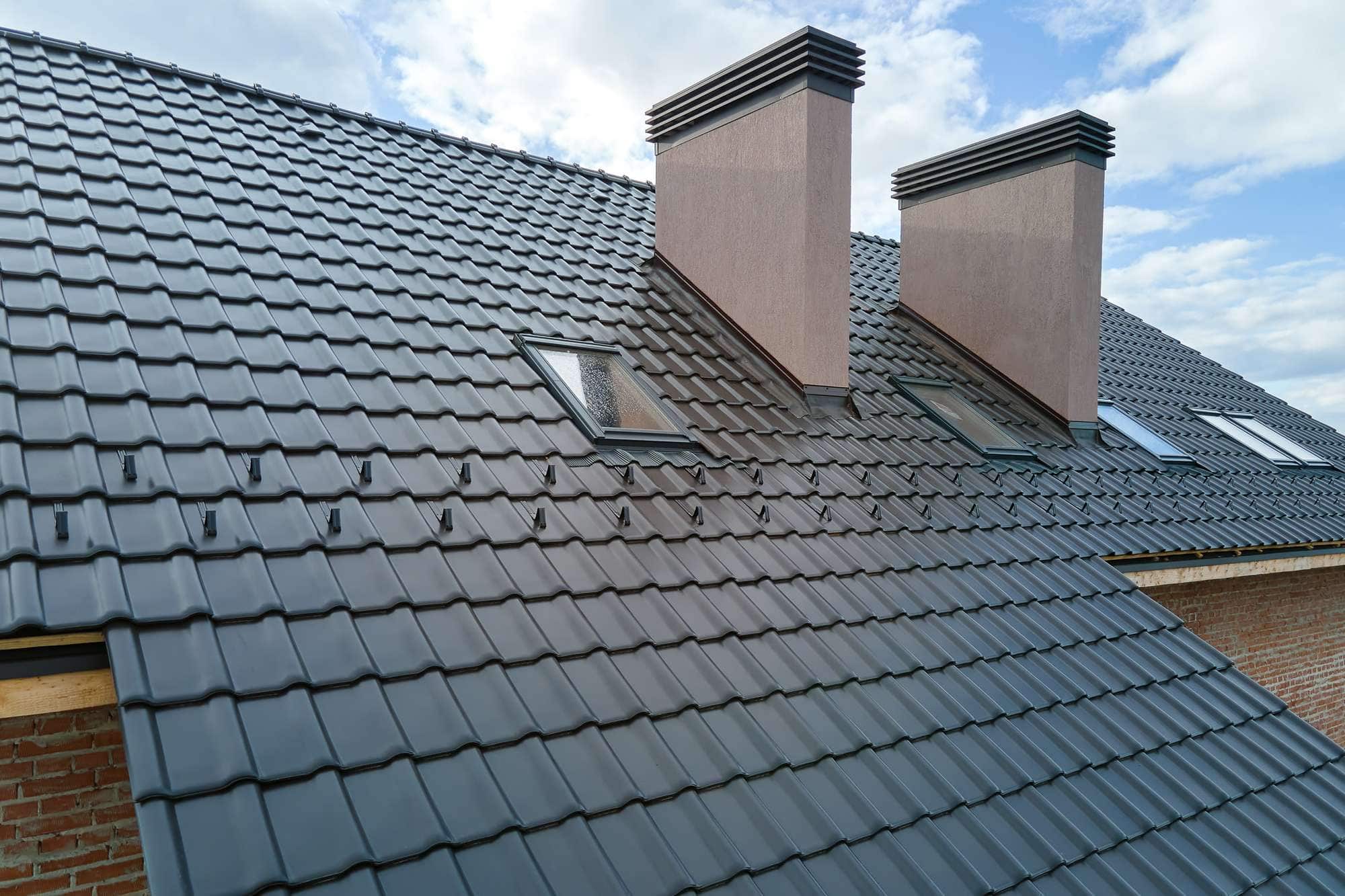 Modern black metal roofing with chimneys and skylights under a cloudy sky; ideal for durability and style.