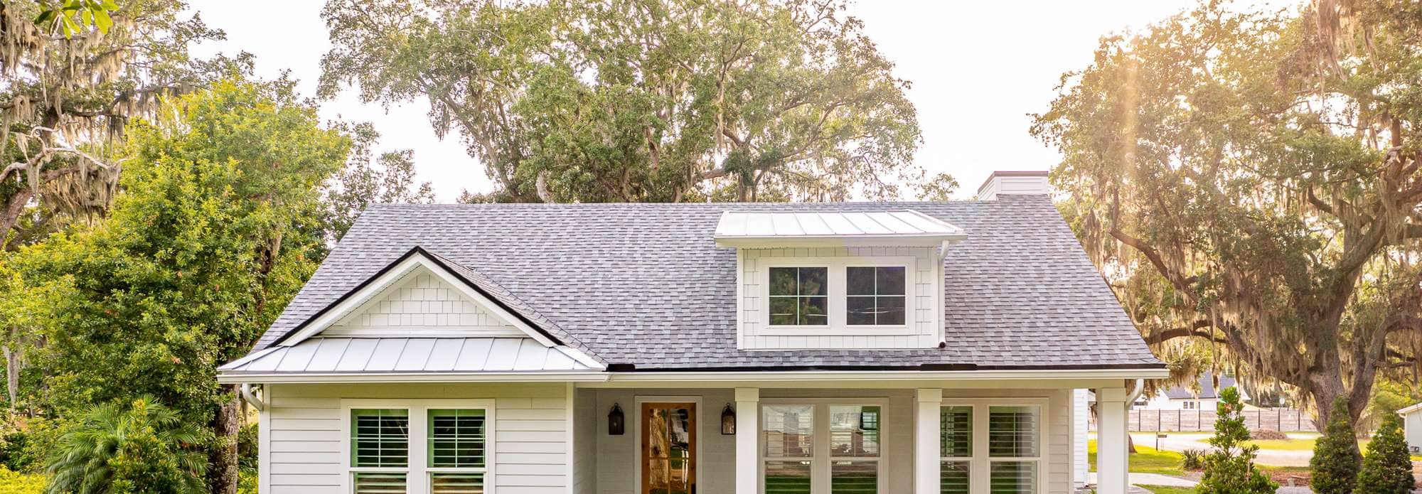 Charming white bungalow with a shingle roof and lush garden backdrop. Ideal for cozy living enthusiasts.