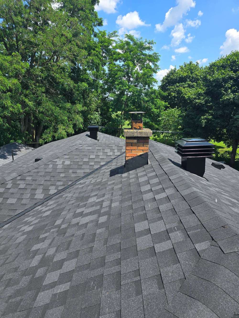 Alt text: Durable asphalt shingle roof with chimney on a sunny day, highlighting quality roofing materials.
