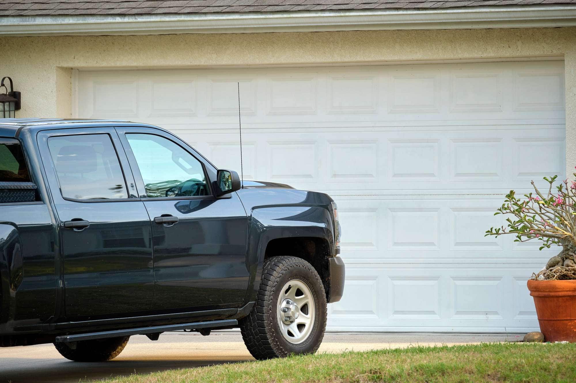Black truck parked in front of a white garage door at a suburban home.